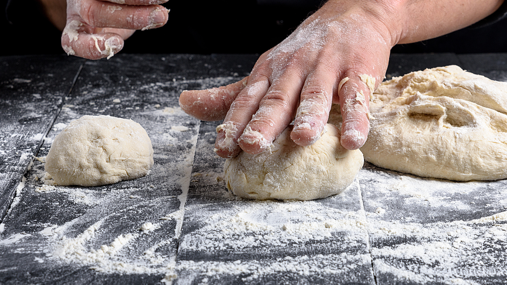 cook making dough balls on a black wooden table, close up