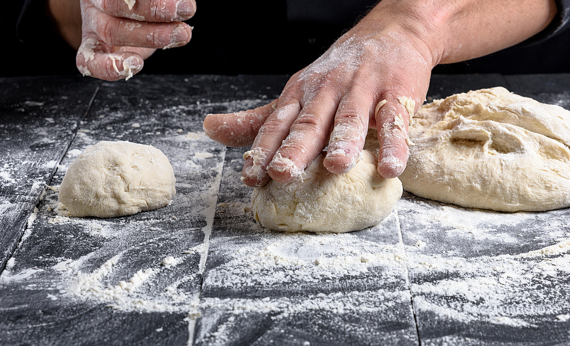 cook making dough balls on a black wooden table, close up